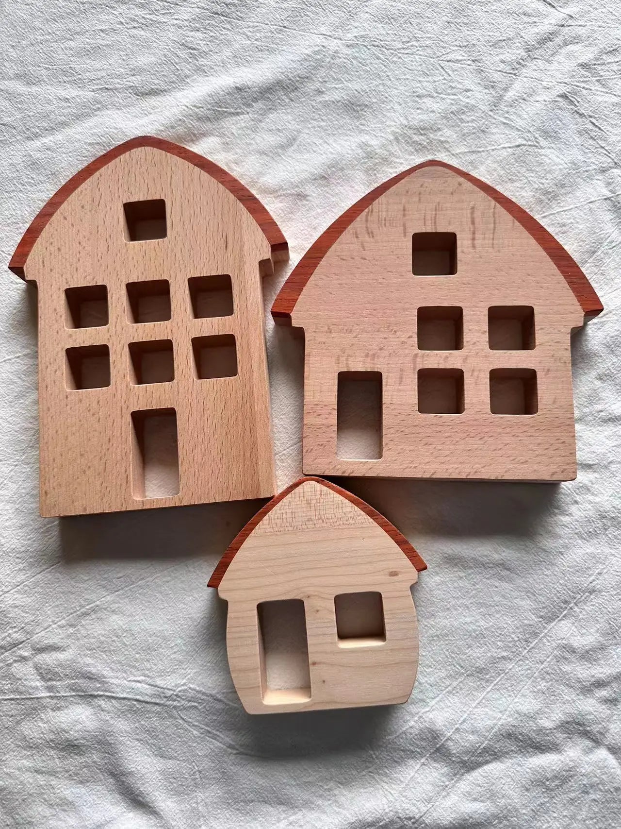 Three wooden house-shaped toys on a textured white surface