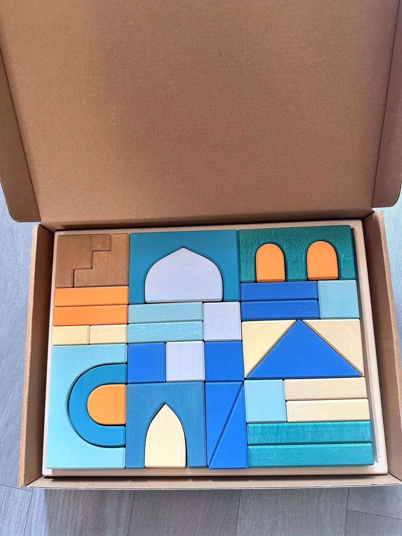 Colorful wooden building blocks in a cardboard box on a light blue surface