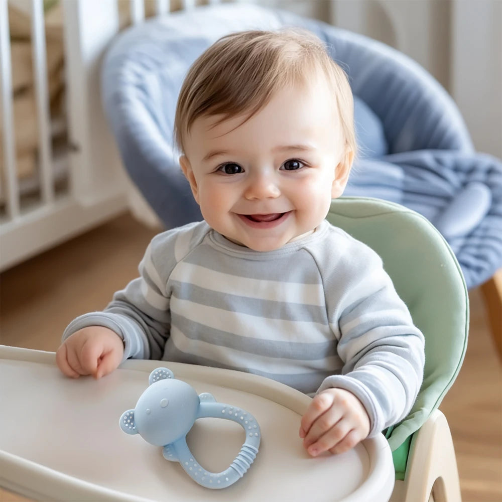 Baby sitting in a high chair with a teething toy, smiling in a nursery setting.