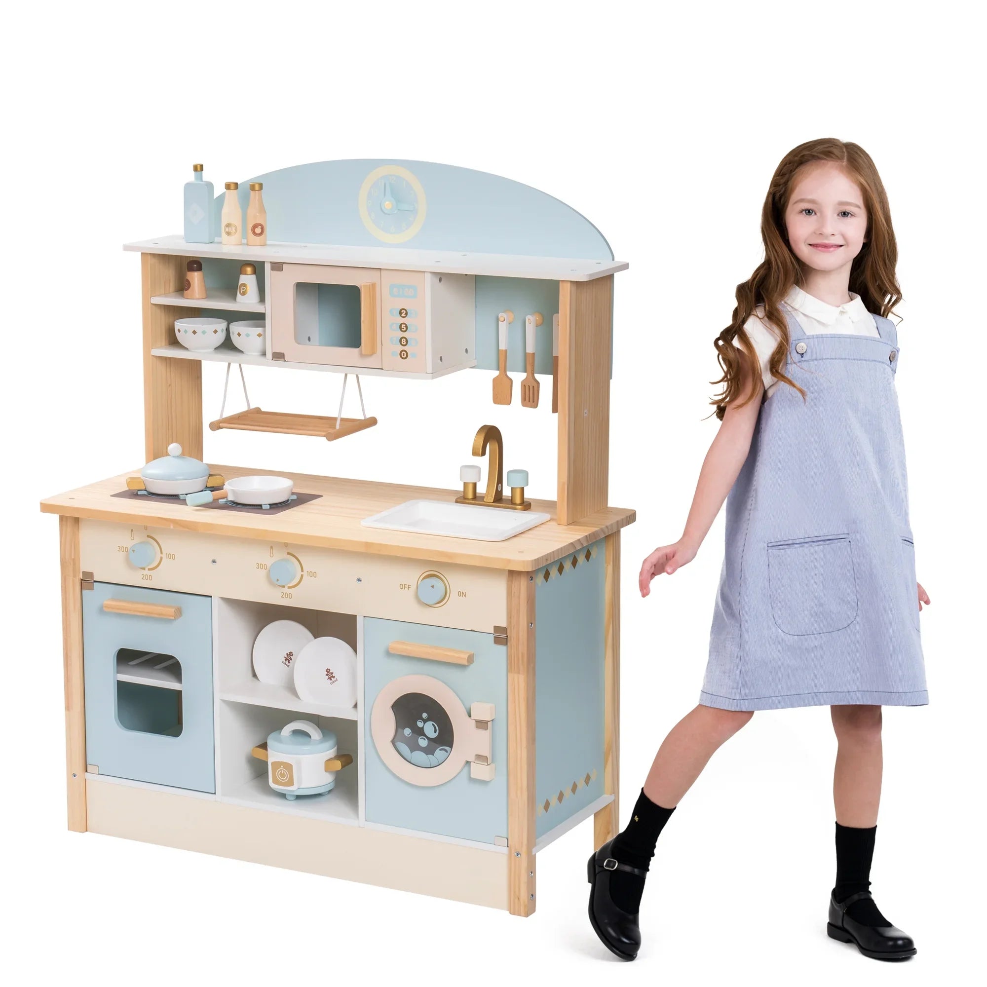 Child-sized wooden play kitchen with a girl in an apron standing next to it on a white background