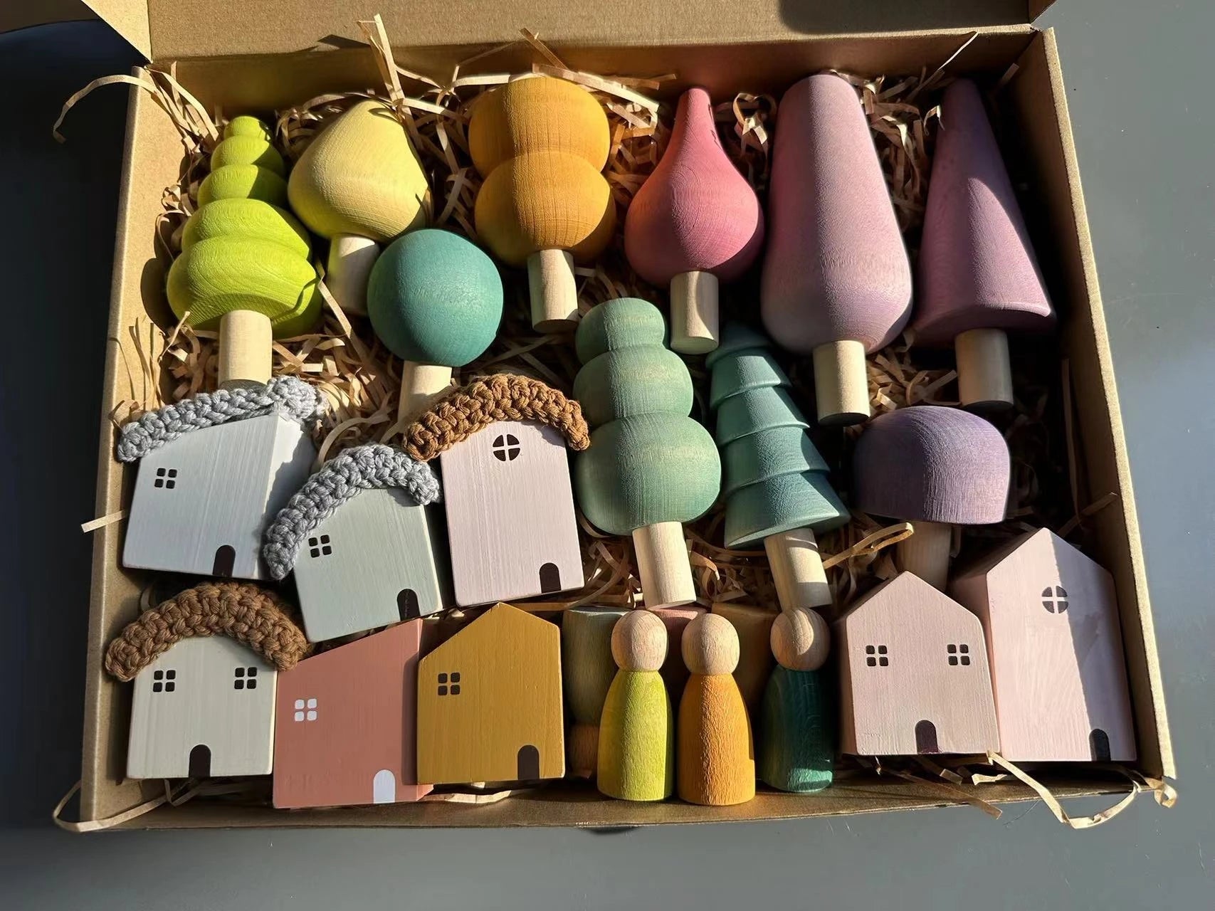 Colorful wooden toys including houses and trees in a box on a gray background
