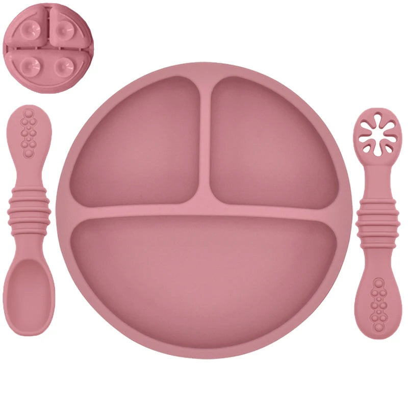 Pink silicone plate with divided sections and four utensils on a white background