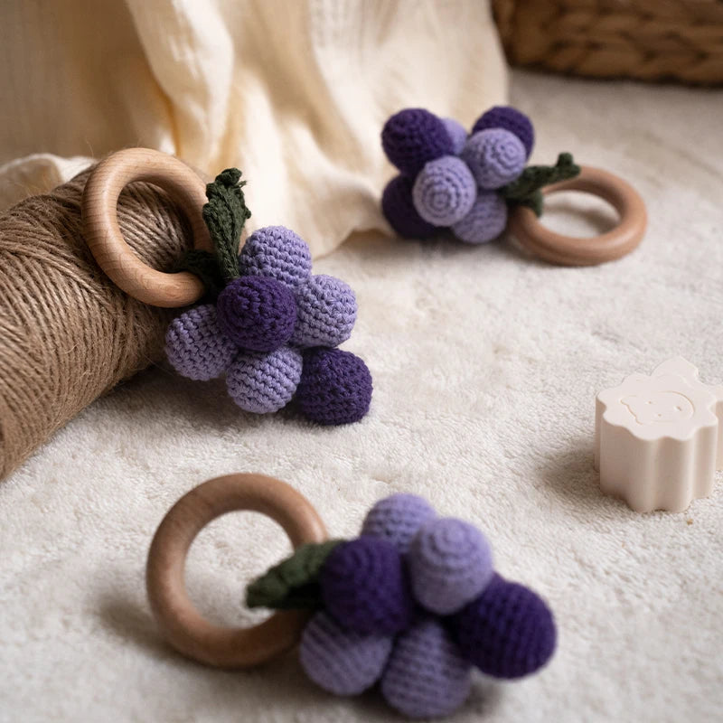 Purple grape-shaped teething rings with wooden rings on a soft surface
