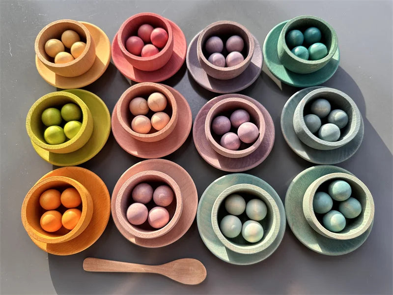 Colorful ceramic bowls with spherical objects and a wooden spoon on a gray background