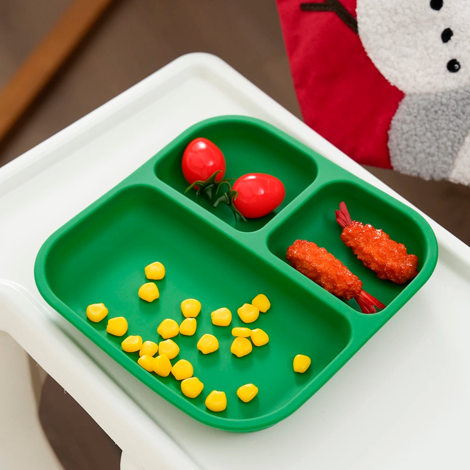 Green square silicone divided plate with strawberries and corn on a high chair tray