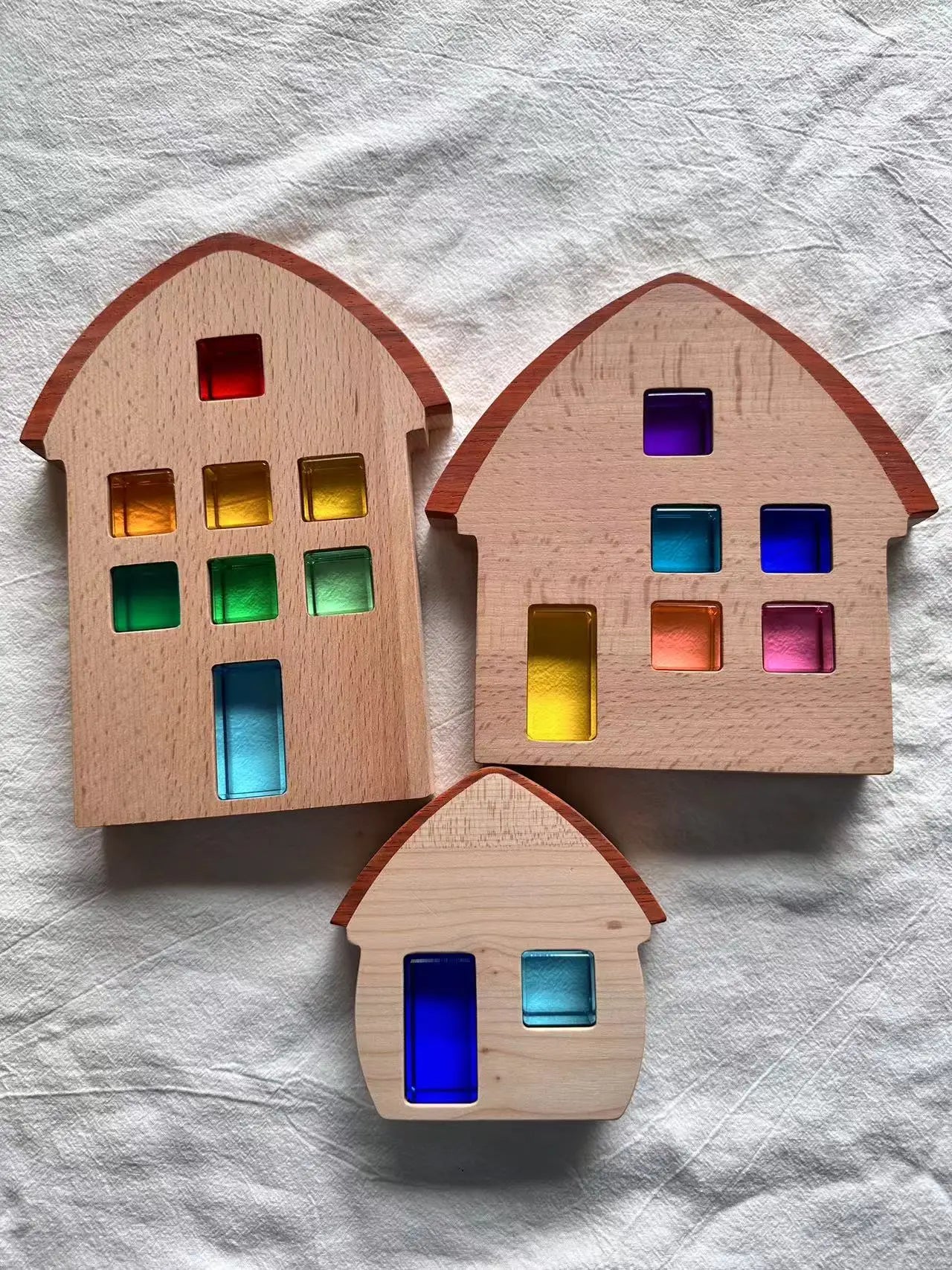 Three wooden house-shaped objects with colored windows on a textured white background