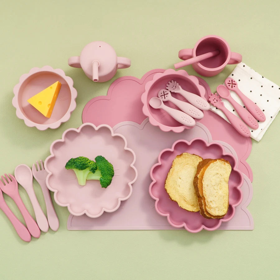 Pink children's dining set with plates, cups, and utensils on a light green background