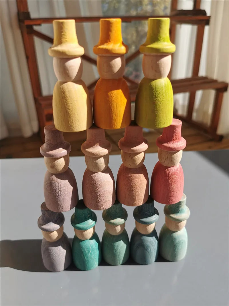 Stack of colorful wooden peg dolls with hats on a white surface.