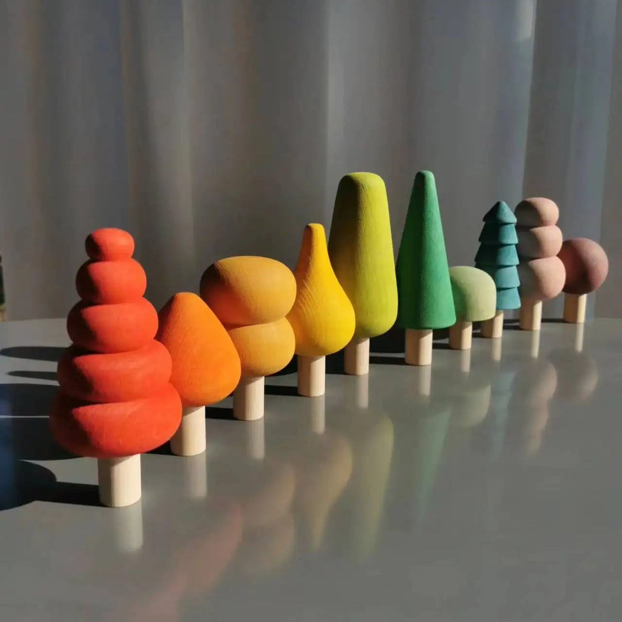 Colorful wooden toy trees arranged in a row on a reflective surface with a neutral background.