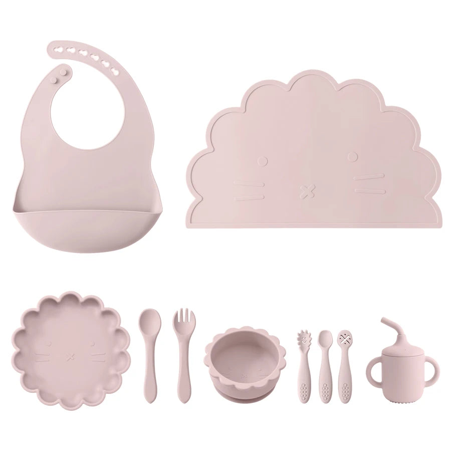 Pink children's dining set including bib, placemat, bowls, utensils, and cup on a white background