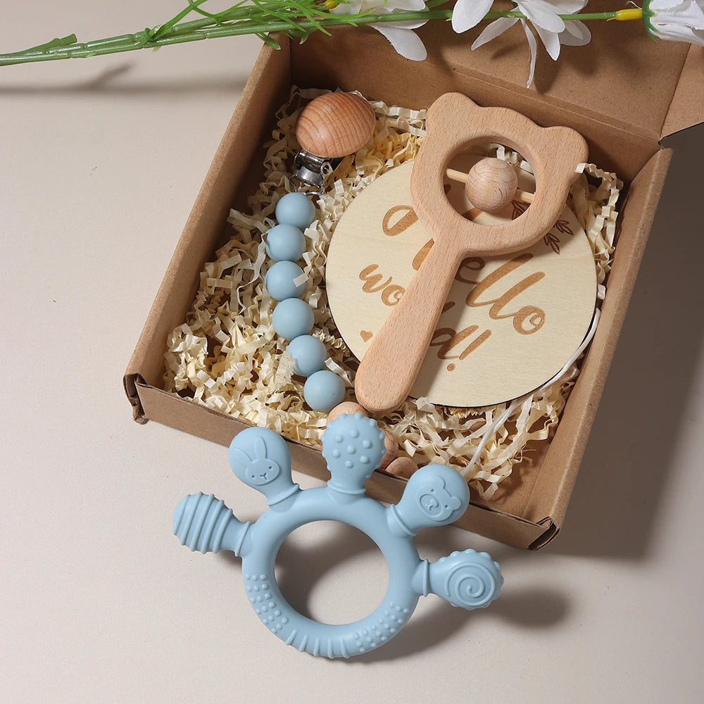 Baby teething toys including a blue rattle and wooden toys in a gift box with flowers.