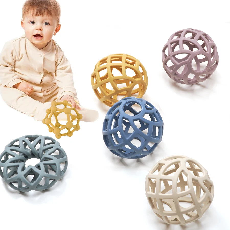 Baby sitting beside silicone lattice teether balls in soft colors