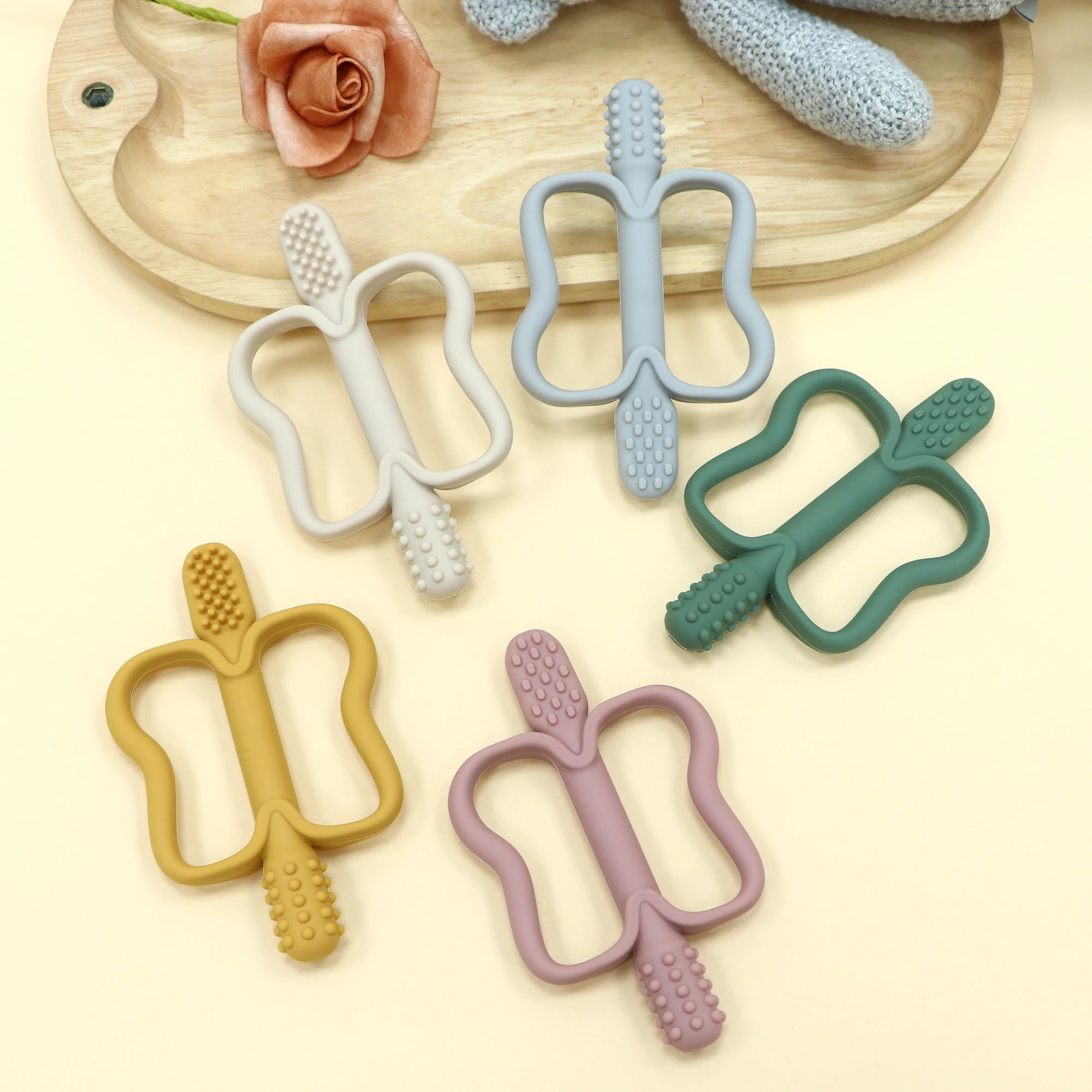 Four colorful baby teething toys on a light yellow background