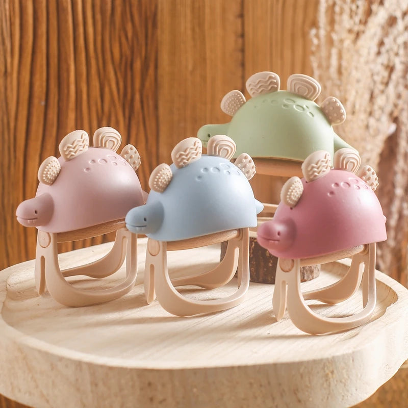 Set of colorful dinosaur-shaped teether toys on a wooden surface with a wooden background.