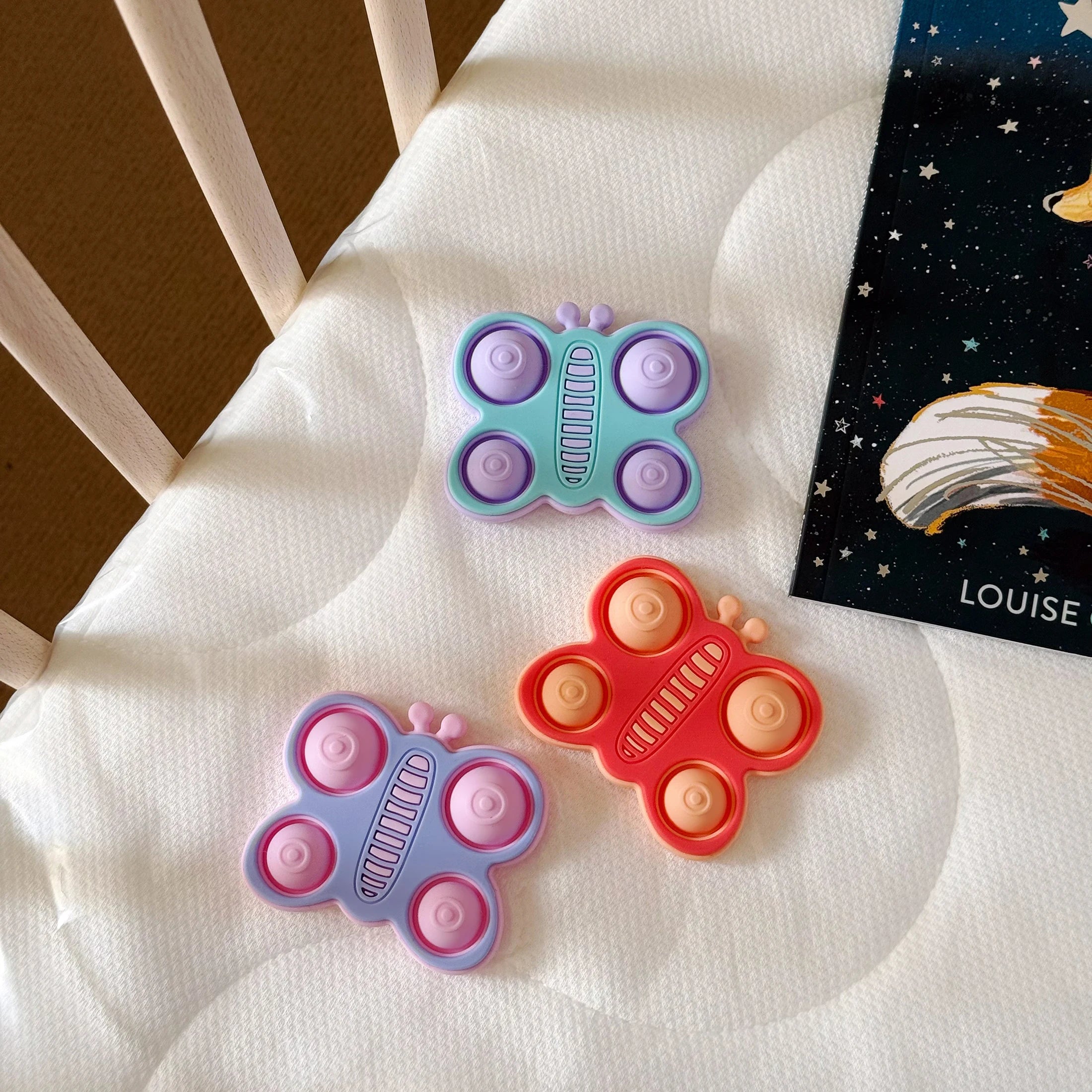 Butterfly pop teethers in purple, coral and mint on a blanket