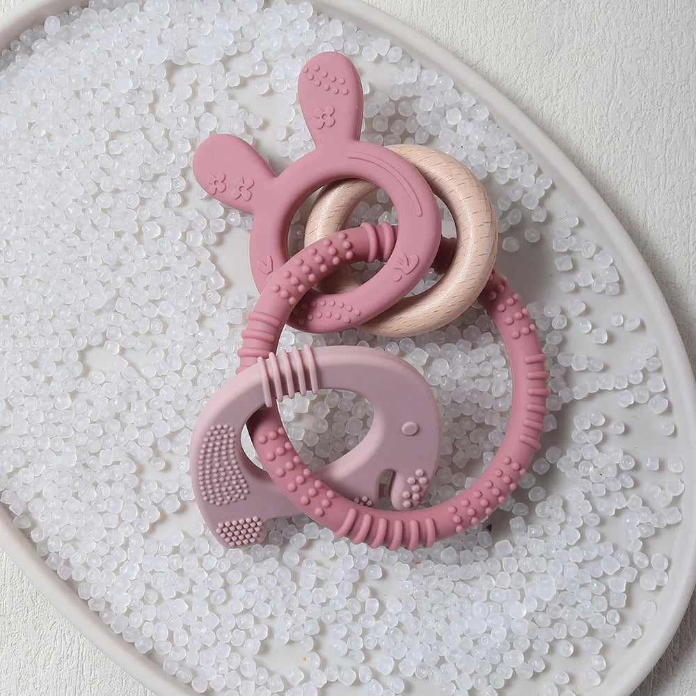 Pink and beige silicone teething rings on a textured white surface