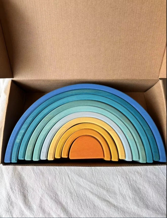 Set of colorful wooden rainbow toys in a cardboard box on a white surface.