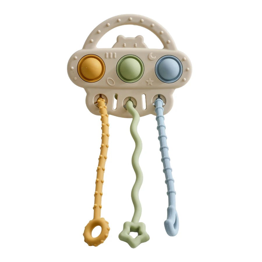 A baby sensory toy with a cream-colored plastic body, featuring three colorful buttons (yellow, green, and blue) and three hanging textured sensory loops in matching pastel colors.