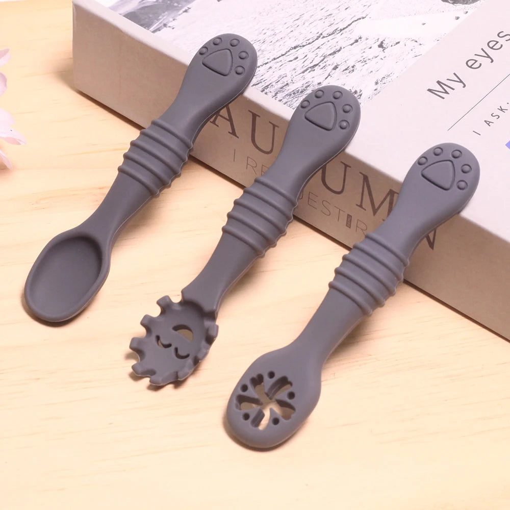 Three gray silicone spoons with unique designs on a light wooden surface.