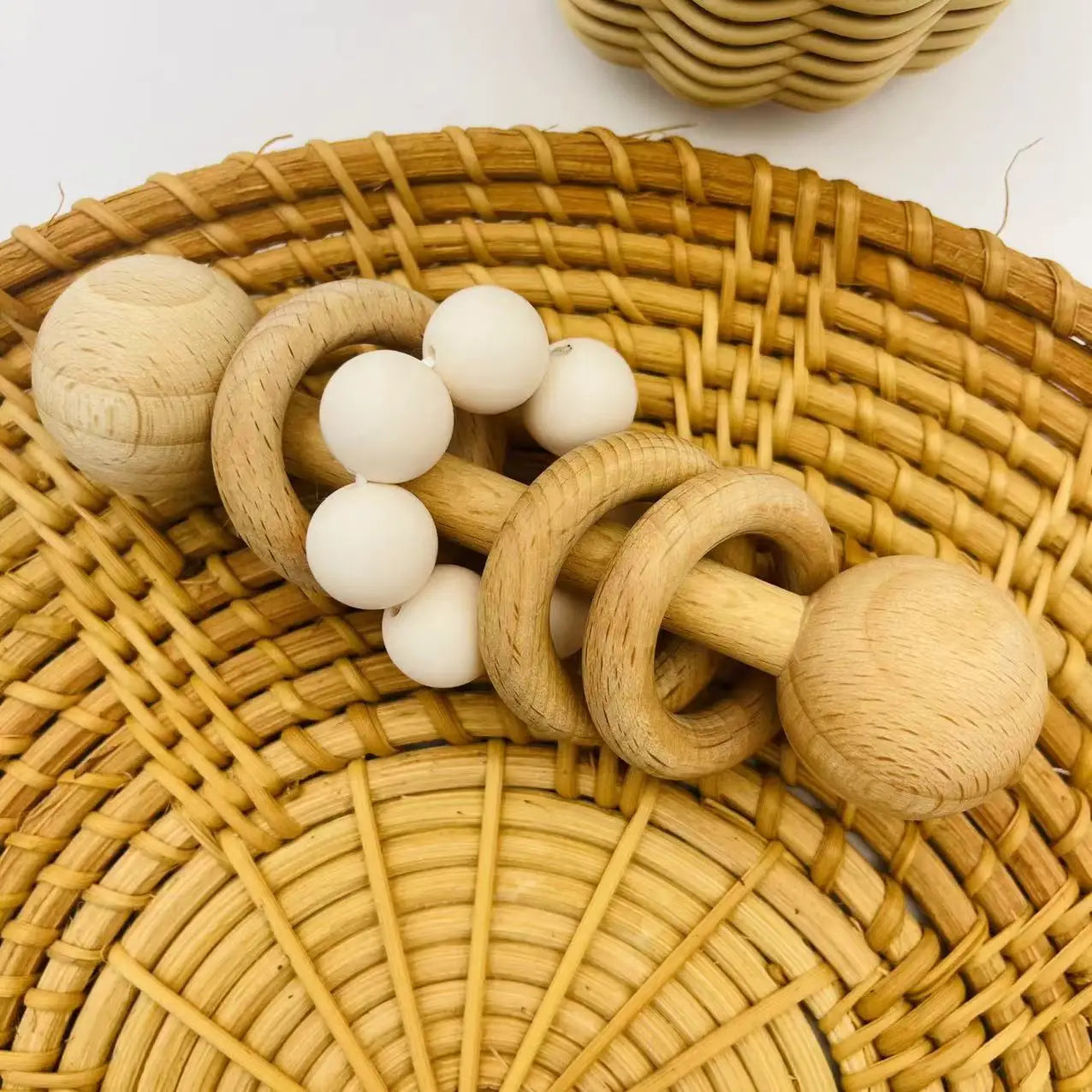 Wooden baby rattle with white beads on a woven surface