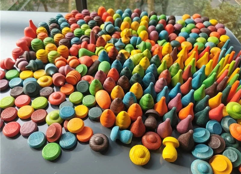 Assorted colorful loose parts toys on a gray surface with a blurred natural background