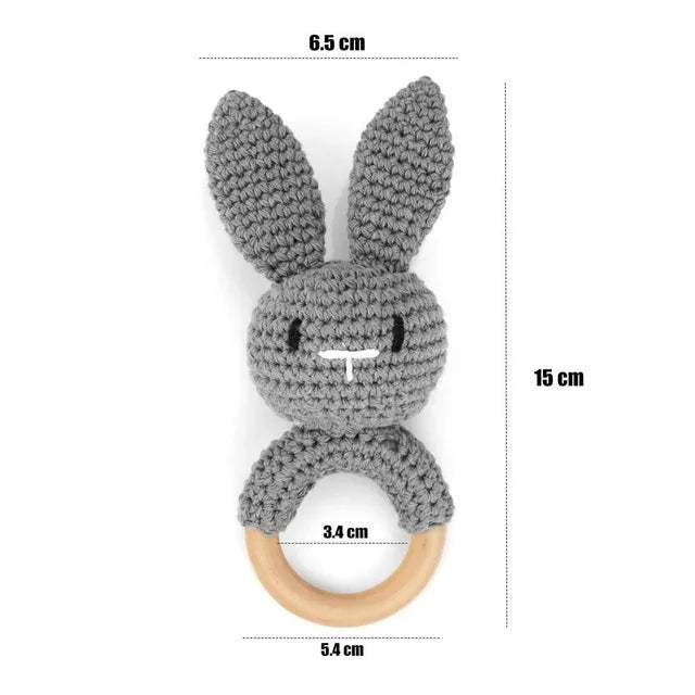 Gray crocheted bunny rattle with wooden ring and measurements on a white background