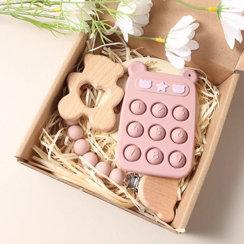 Pink baby teether with wooden flower and round beads in a decorative box with flowers.
