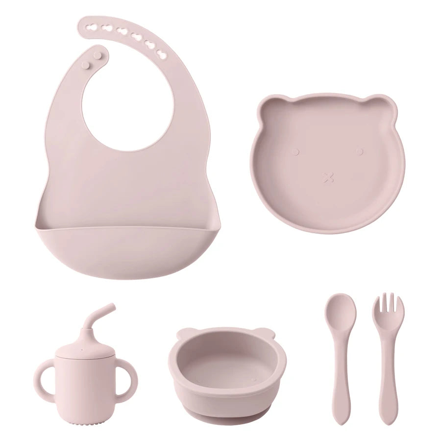 Pink baby feeding set including bib, plate, cup, bowl, spoon, and fork on a white background