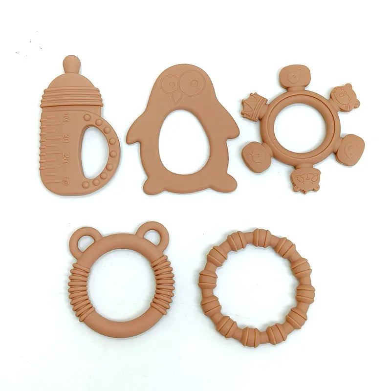 Five natural silicone baby teething toys in a uniform light brown color, arranged on a plain white background. The set includes a bottle-shaped teether, an owl-shaped teether, a flower-shaped teether with animal faces, a bear-shaped textured ring, and a bamboo-style textured ring.