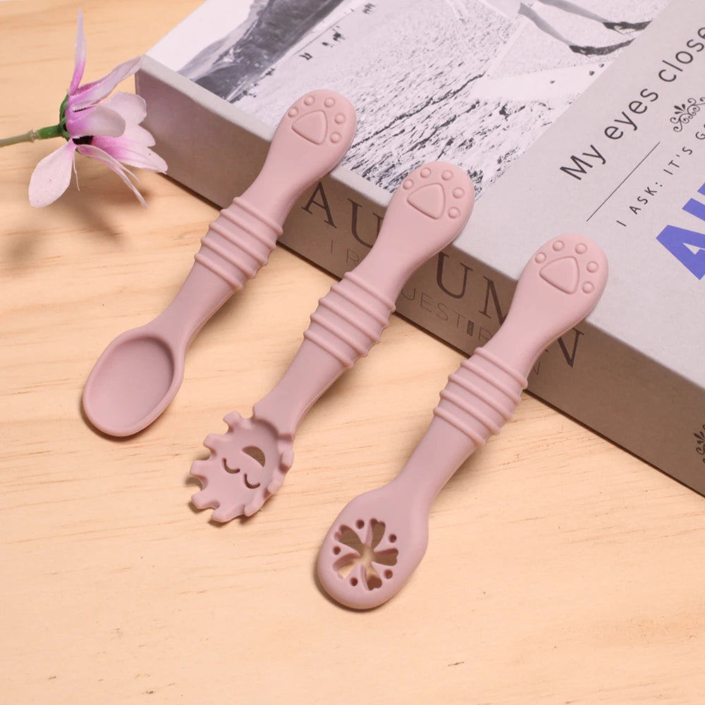 Two pink baby spoons with unique designs on a wooden surface.