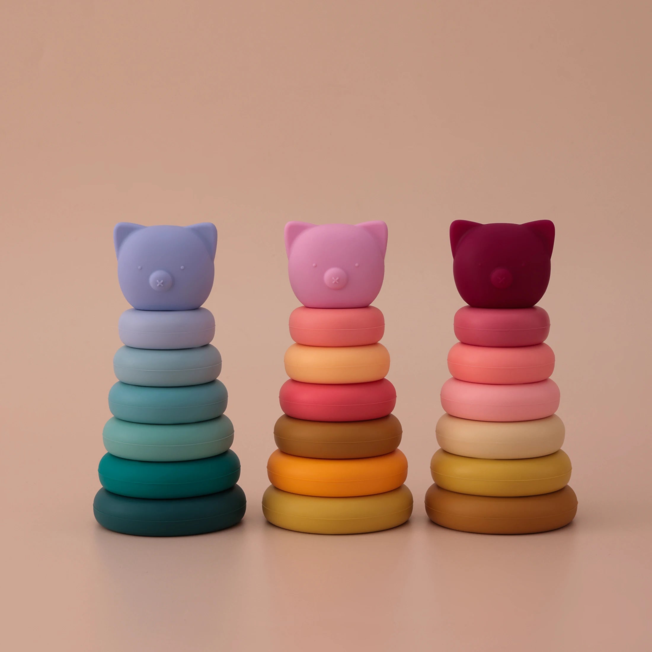 Three colorful cat-shaped ring stacks on a beige background