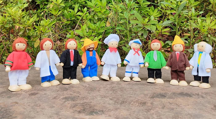 Row of colorful figurines with different outfits on a wooden surface with greenery in the background