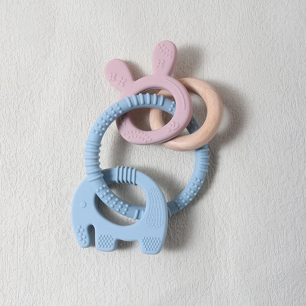 Set of three silicone teething rings in pink, blue, and beige on a light gray background