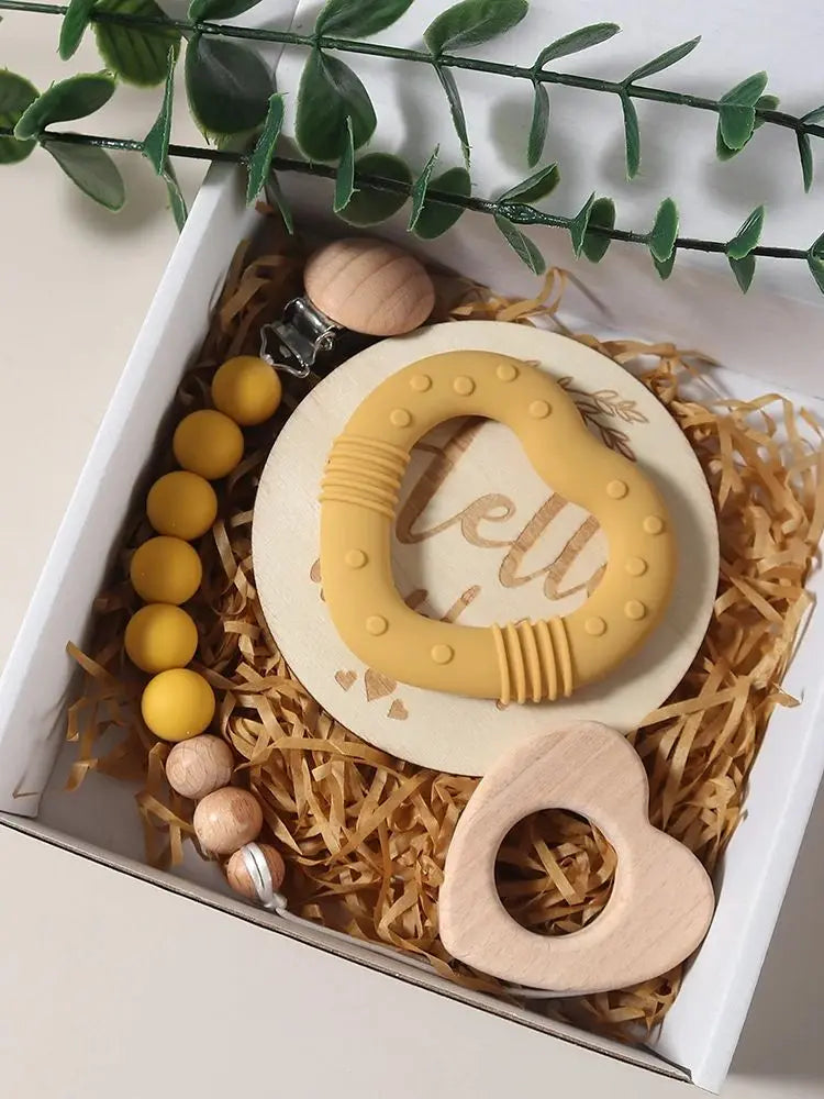 Yellow and wooden baby teething toys in a decorative box with greenery.