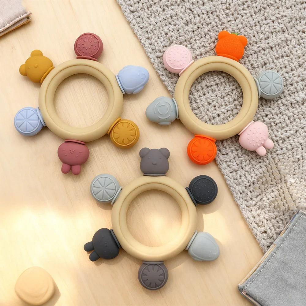 Colorful baby teething rings with various animal-shaped ends on a textured surface.