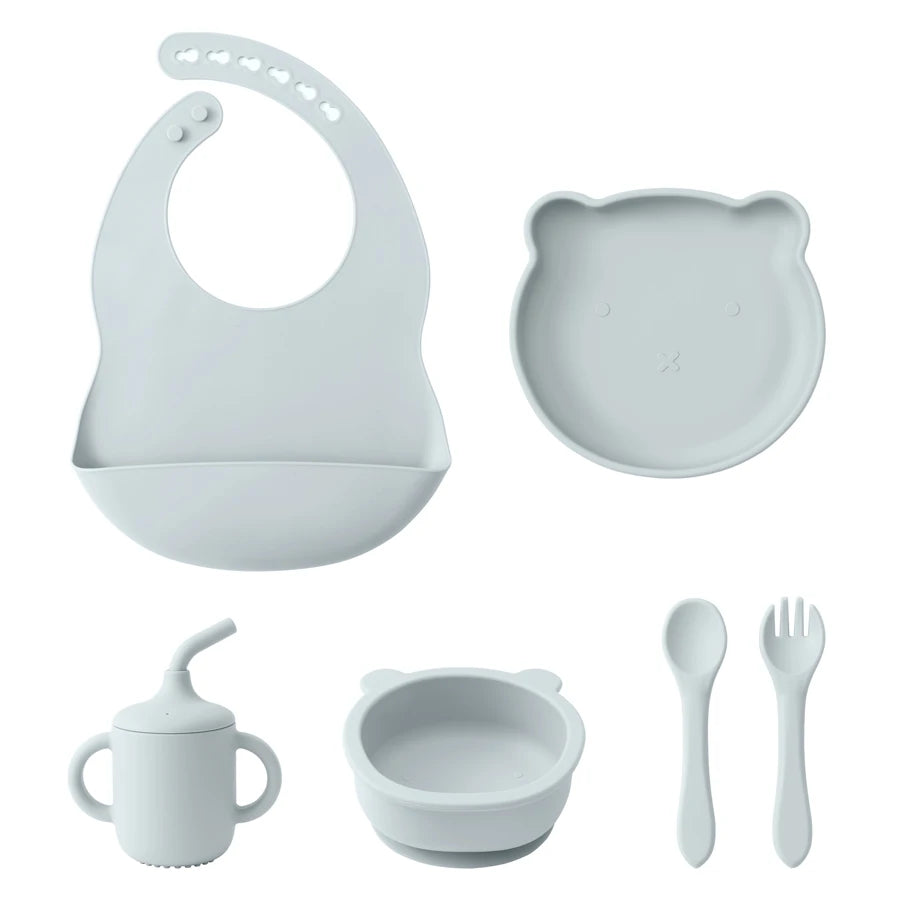 Set of baby feeding utensils including a bib, bowl, cup, spoon, and fork on a white background.