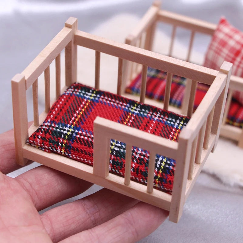 Miniature wooden crib with plaid bedding held in a hand against a neutral background