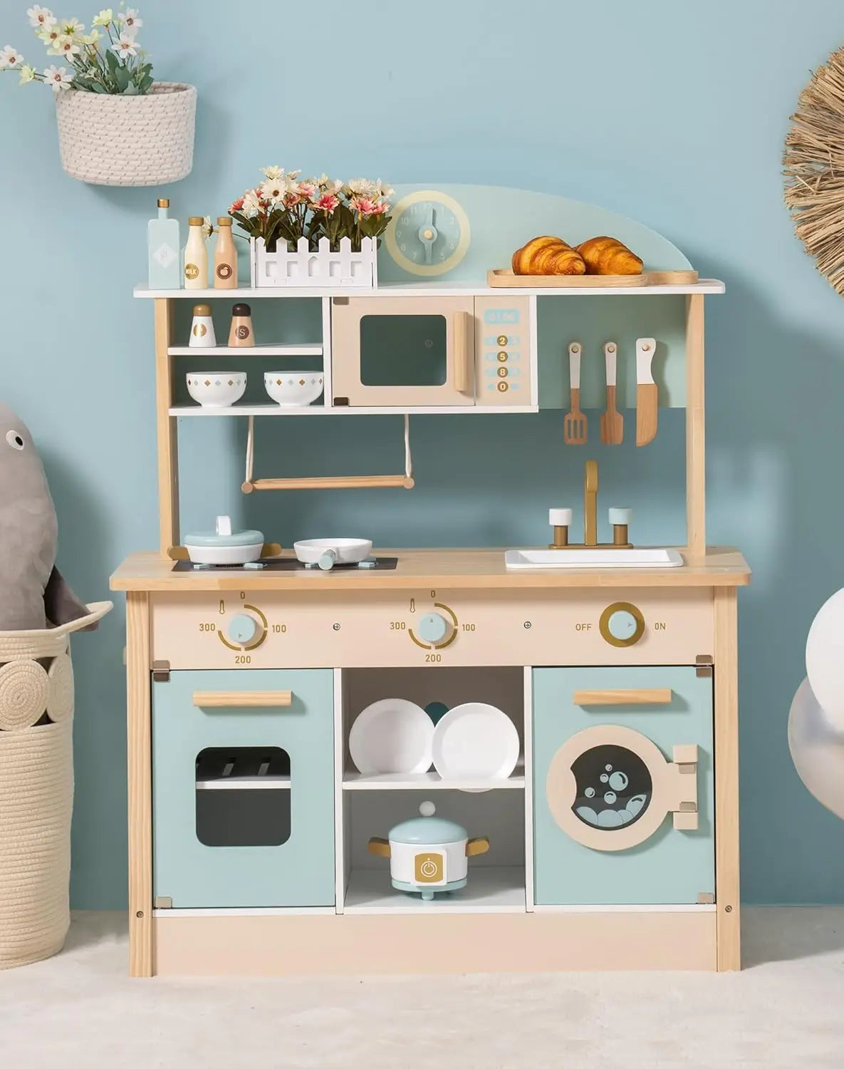 Children's wooden play kitchen set against a light blue wall with decorative elements.