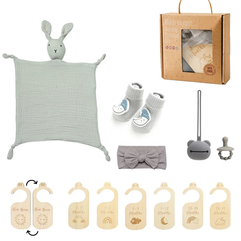 Collection of baby items including a green plush toy, booties, a pacifier, a headband, and wooden baby toys on a white background.