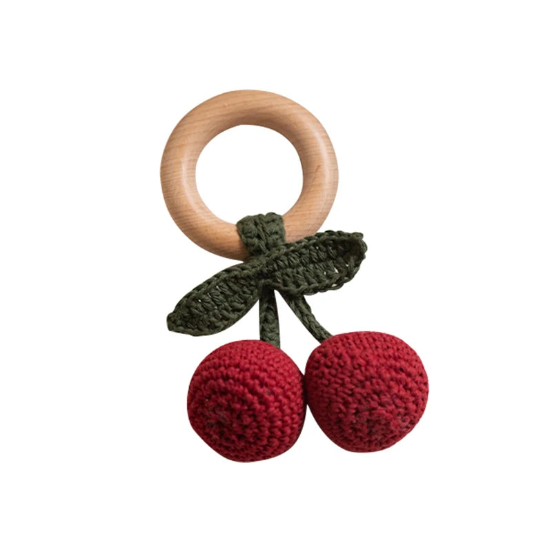 Wooden teething ring with red crocheted cherries and green leaves on a white background