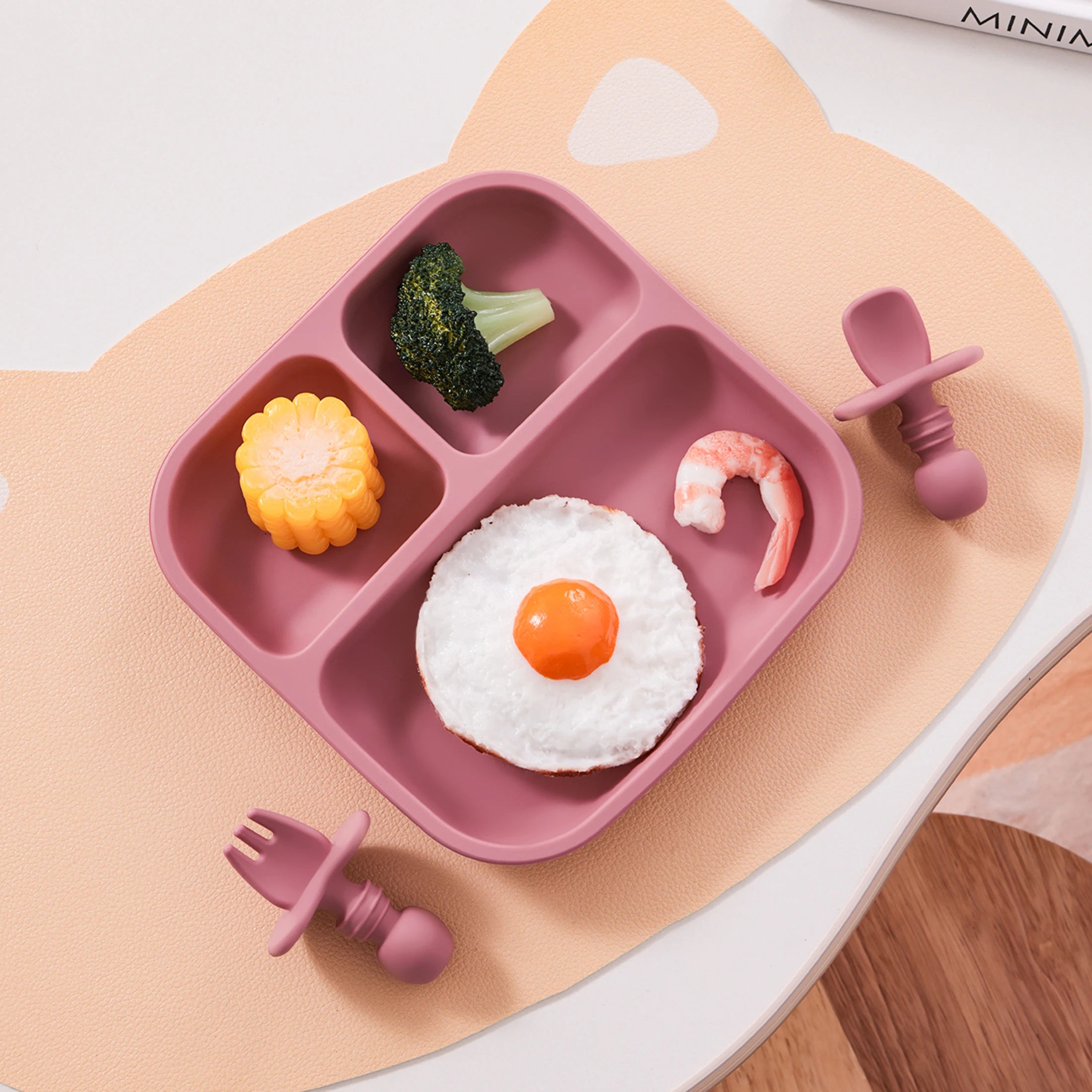 Pink children's meal tray with food and utensils on a white surface