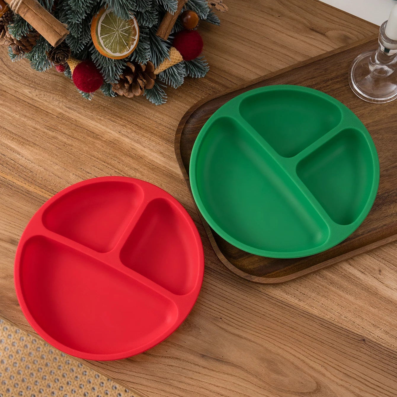 Red and green round silicone divided plates on a wooden table with holiday decor