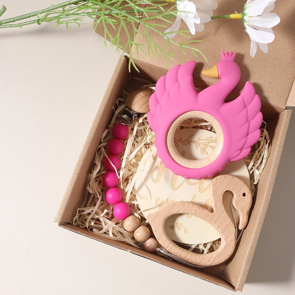 Pink and wooden swan-shaped teething toys in a box with flowers in the background