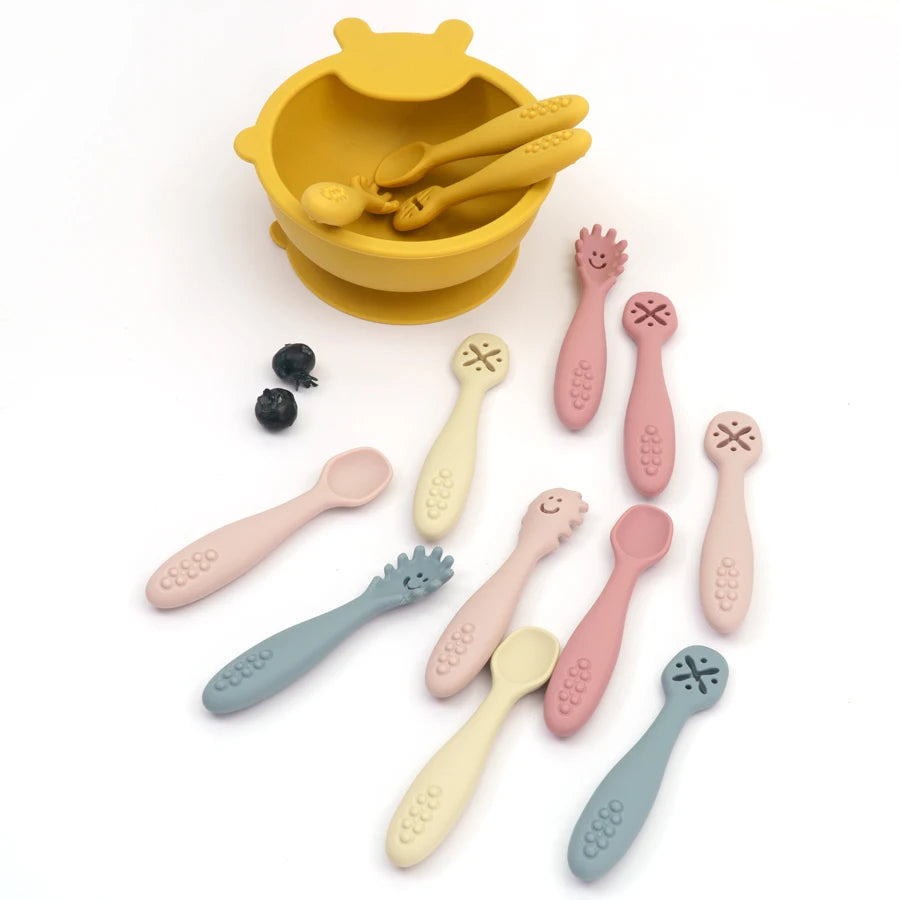 Silicone learning spoons in pastel colors beside a yellow suction bowl