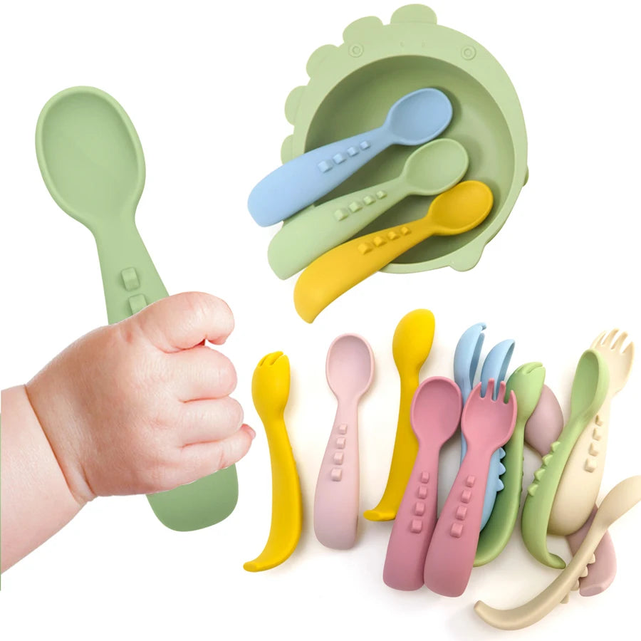 Baby holding a green silicone spoon beside spoon and fork sets