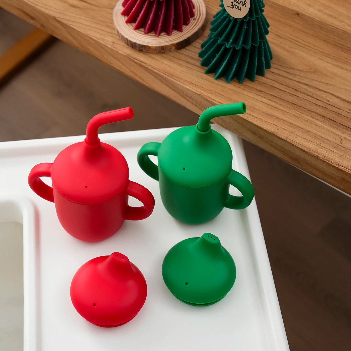 Red and green silicone sippy and straw cups on a high chair tray
