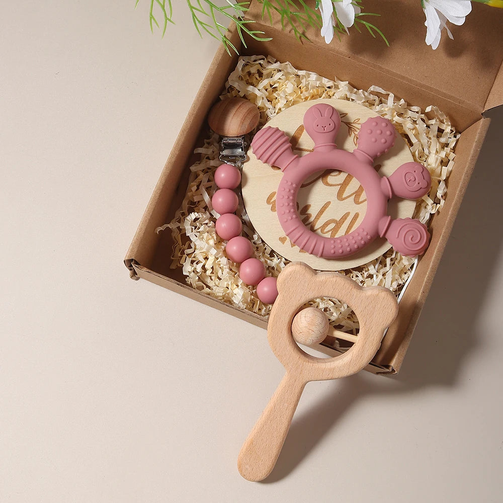 Set of baby teething toys including a pink and wooden rattle in a box.