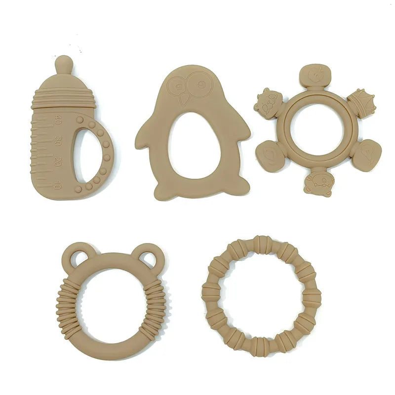 Five beige silicone baby teething toys in different shapes, including a bottle, penguin, flower, bear, and textured ring, arranged on a plain white background.