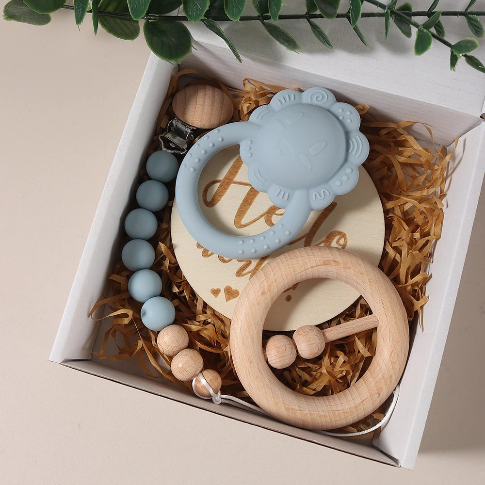 Set of baby teething rings and beads in a decorative box with a plant in the background.