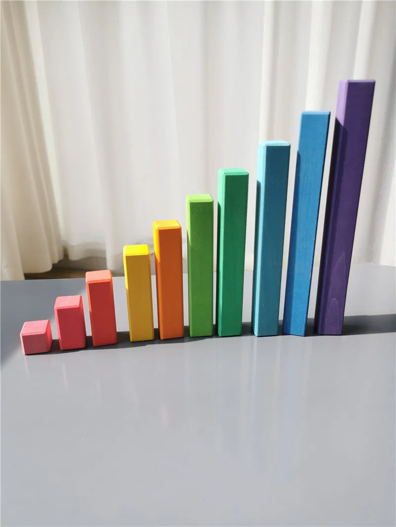 Colorful wooden blocks arranged in a gradient on a white surface with a white curtain background.